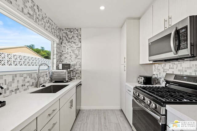 kitchen featuring decorative backsplash, sink, appliances with stainless steel finishes, and light hardwood / wood-style flooring