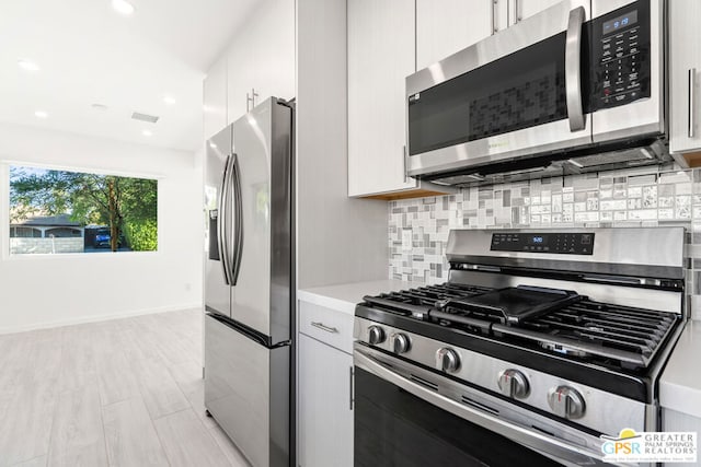 kitchen featuring backsplash, light wood-type flooring, white cabinetry, and stainless steel appliances