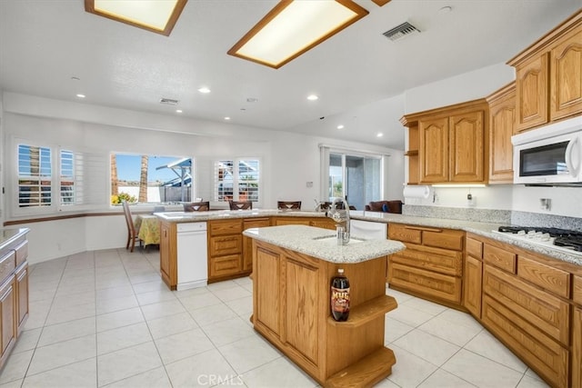 kitchen featuring light tile patterned floors, kitchen peninsula, sink, white appliances, and a center island