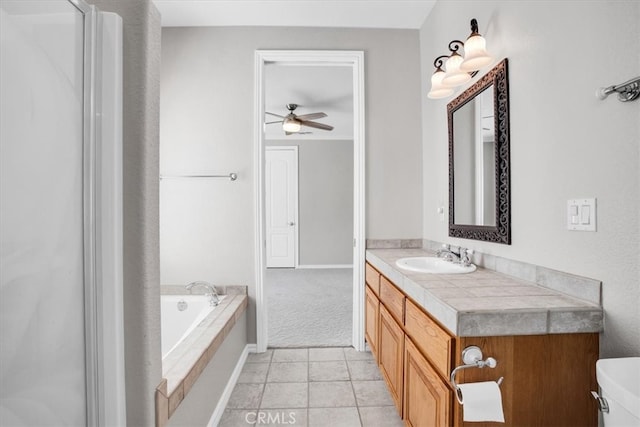 bathroom featuring tiled tub, vanity, tile patterned flooring, ceiling fan, and toilet