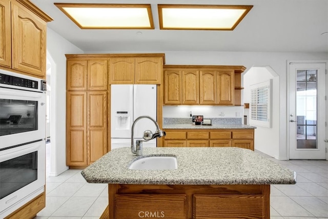 kitchen with a center island with sink, white appliances, sink, and light tile patterned floors