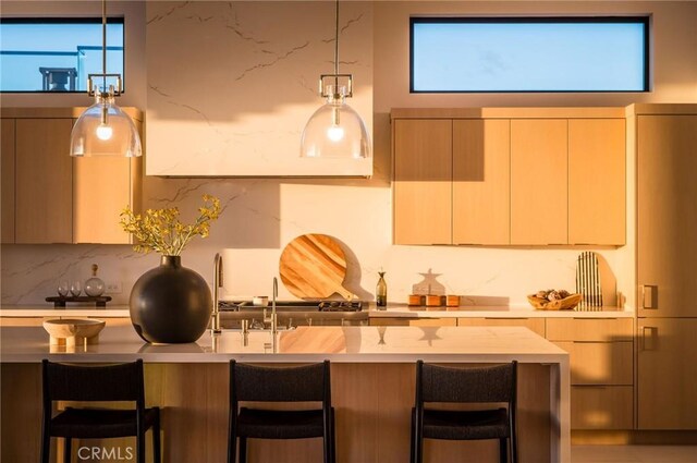 kitchen featuring pendant lighting, backsplash, light brown cabinets, and a kitchen bar