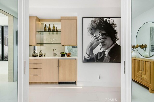 bar featuring backsplash, light brown cabinets, light tile patterned floors, and sink