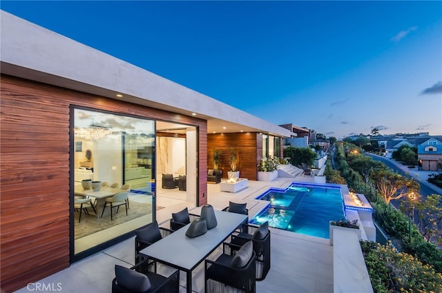 pool at dusk featuring an in ground hot tub, a patio area, and pool water feature