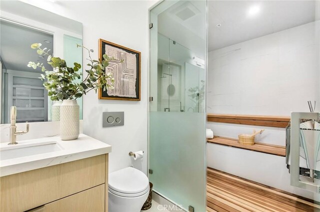 bathroom with a shower with shower door, vanity, and toilet