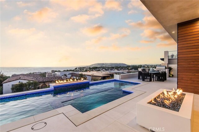 pool at dusk featuring a water view, a patio area, and a fire pit