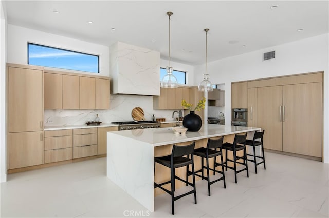 kitchen with tasteful backsplash, a kitchen island with sink, light brown cabinets, and plenty of natural light