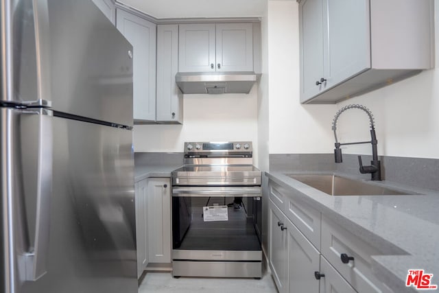 kitchen featuring appliances with stainless steel finishes, light stone countertops, gray cabinets, exhaust hood, and sink