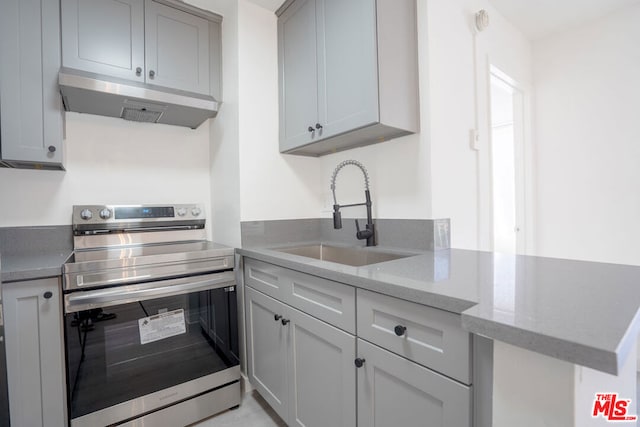 kitchen featuring light stone counters, kitchen peninsula, stainless steel range with electric stovetop, gray cabinets, and sink