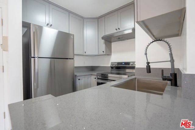 kitchen with appliances with stainless steel finishes, gray cabinets, sink, and light stone counters