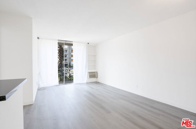 unfurnished room featuring built in shelves and light hardwood / wood-style floors