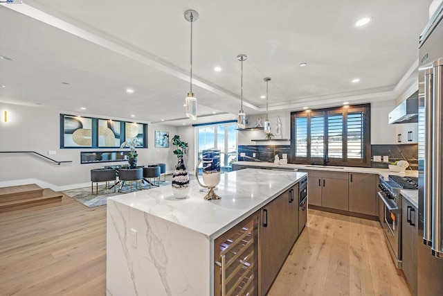 kitchen featuring light hardwood / wood-style floors, light stone counters, a center island, decorative light fixtures, and stainless steel range