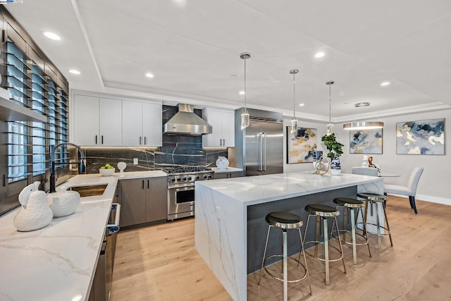 kitchen with wall chimney exhaust hood, premium appliances, pendant lighting, a center island, and sink