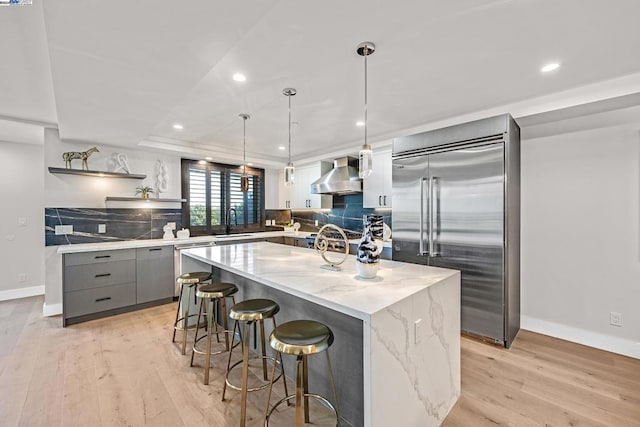 kitchen featuring gray cabinetry, light hardwood / wood-style floors, built in refrigerator, wall chimney exhaust hood, and a center island