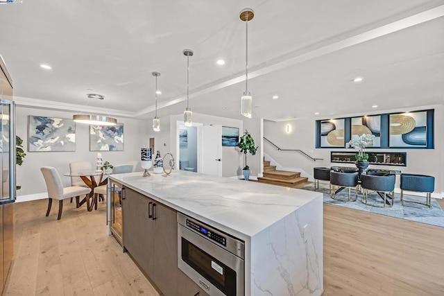 kitchen with pendant lighting, light stone counters, light hardwood / wood-style flooring, and a large island with sink