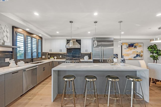 kitchen featuring stainless steel appliances, wall chimney range hood, decorative light fixtures, and sink