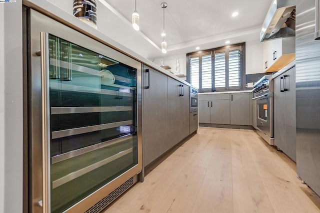 kitchen with light hardwood / wood-style floors, beverage cooler, hanging light fixtures, wall chimney exhaust hood, and appliances with stainless steel finishes