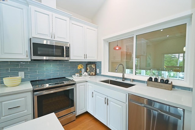 kitchen with white cabinets, sink, backsplash, stainless steel appliances, and light wood-type flooring