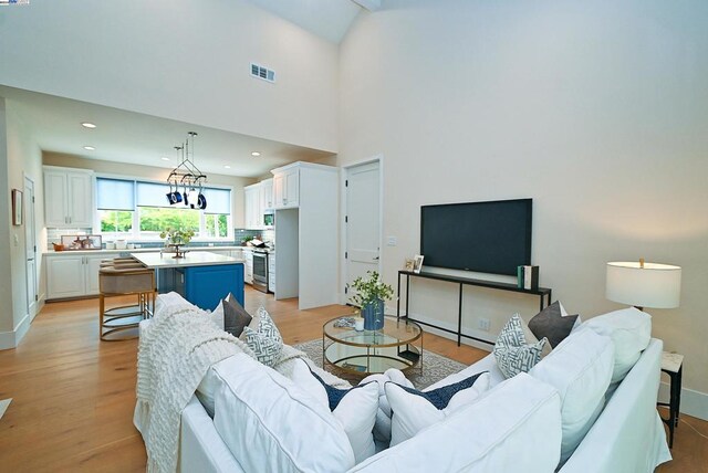 living room with a notable chandelier, light wood-type flooring, and a high ceiling