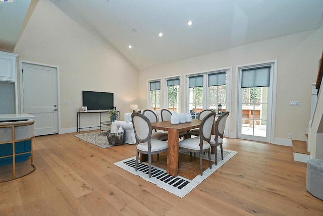 dining room with light wood-type flooring and high vaulted ceiling