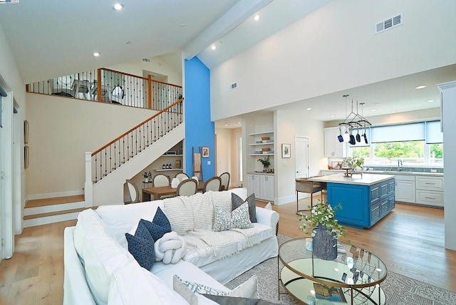 living room featuring a notable chandelier, light hardwood / wood-style floors, high vaulted ceiling, and sink