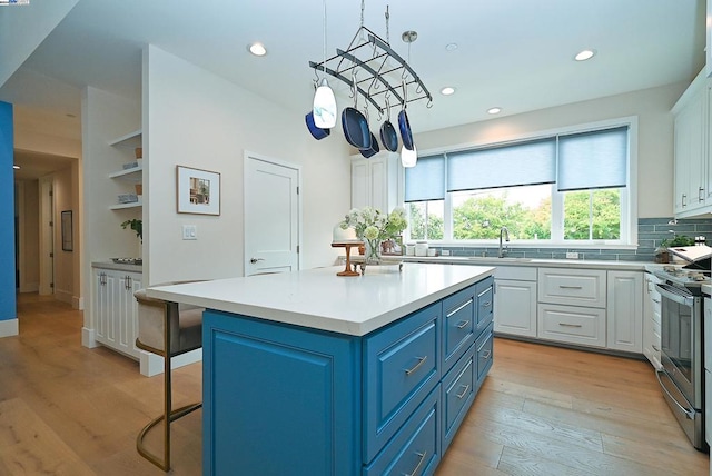 kitchen with light hardwood / wood-style floors, white cabinets, a kitchen island, blue cabinetry, and electric range