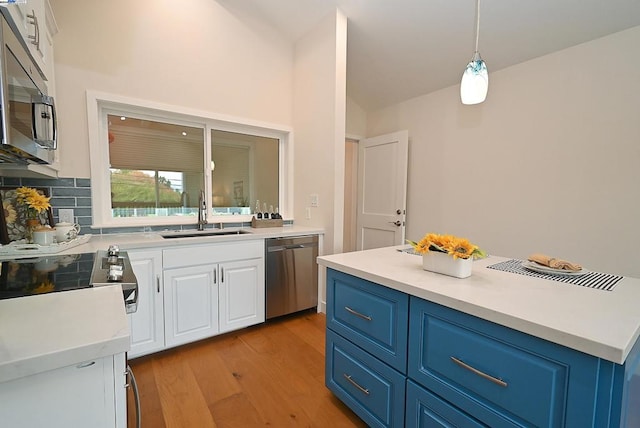 kitchen featuring appliances with stainless steel finishes, hanging light fixtures, light hardwood / wood-style floors, white cabinets, and sink