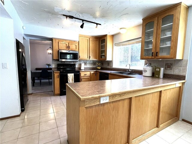 kitchen with light tile patterned floors, sink, kitchen peninsula, backsplash, and black appliances