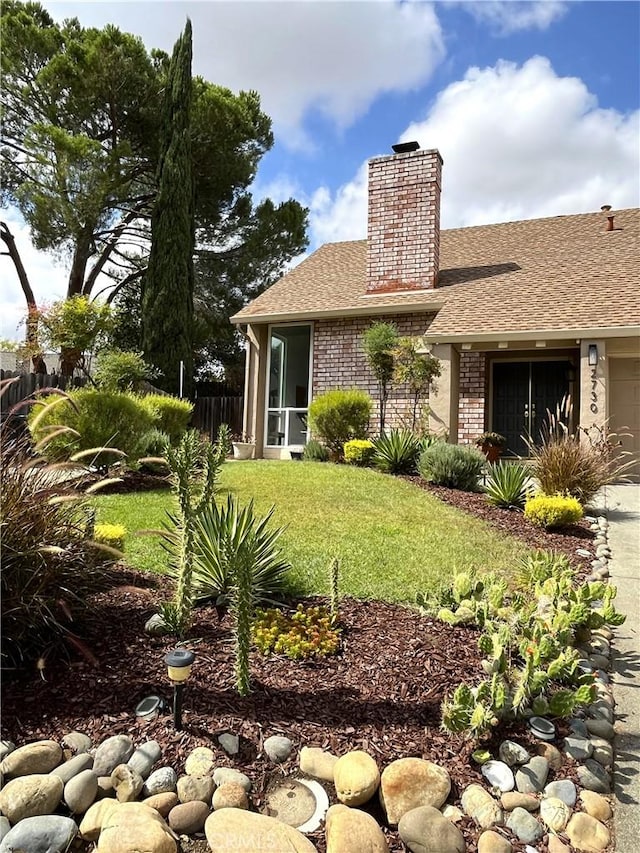back of house featuring fence, a chimney, brick siding, a shingled roof, and a yard