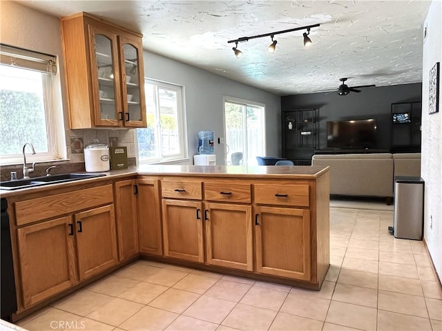 kitchen with brown cabinetry, rail lighting, a sink, light tile patterned floors, and a peninsula