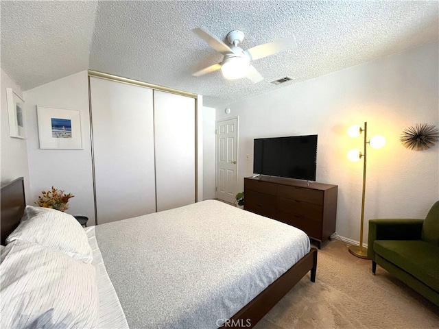 bedroom featuring visible vents, a closet, ceiling fan, light colored carpet, and a textured ceiling