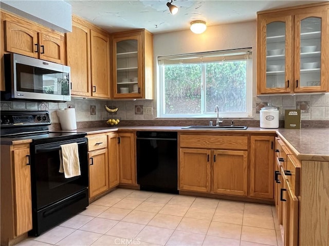 kitchen with light tile patterned flooring, a sink, decorative backsplash, glass insert cabinets, and black appliances