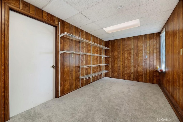 carpeted empty room featuring wooden walls and a drop ceiling