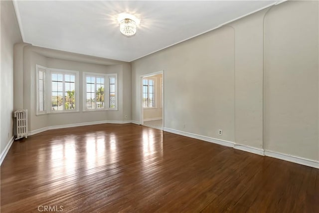 spare room with dark wood-type flooring, radiator, and a chandelier