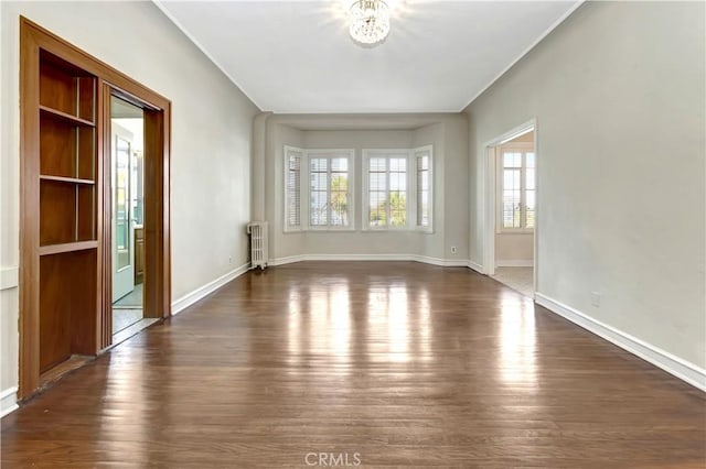 unfurnished room featuring a notable chandelier, dark hardwood / wood-style floors, a healthy amount of sunlight, and radiator