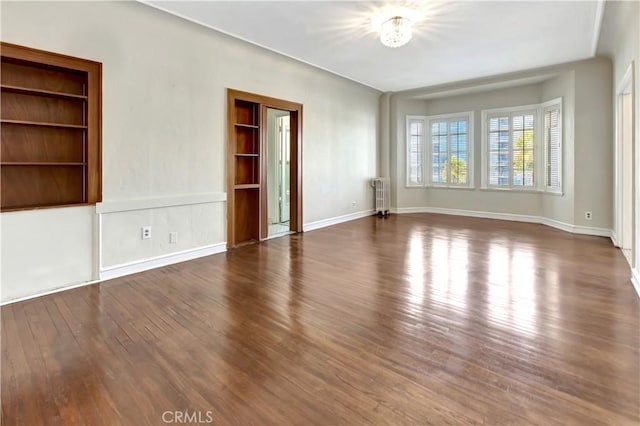 empty room with radiator, dark hardwood / wood-style flooring, built in shelves, and a notable chandelier