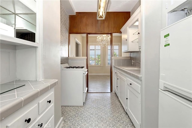 kitchen featuring white gas stove, tile counters, refrigerator, decorative backsplash, and white cabinets