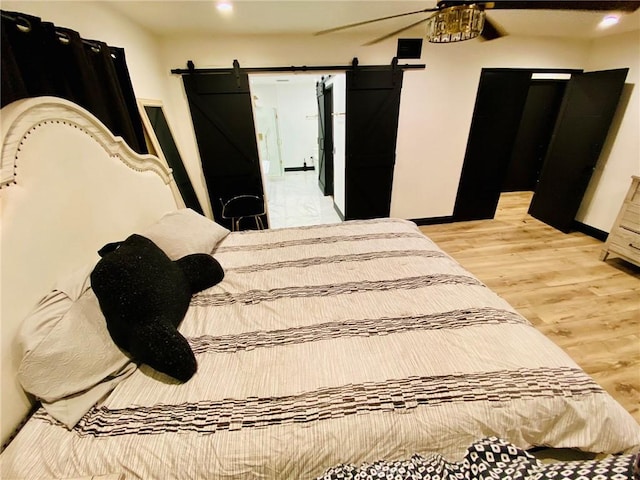 bedroom with a barn door, ceiling fan, and light wood-type flooring