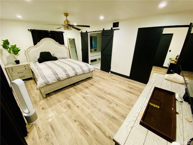 bedroom featuring ceiling fan, a barn door, light wood-type flooring, and connected bathroom