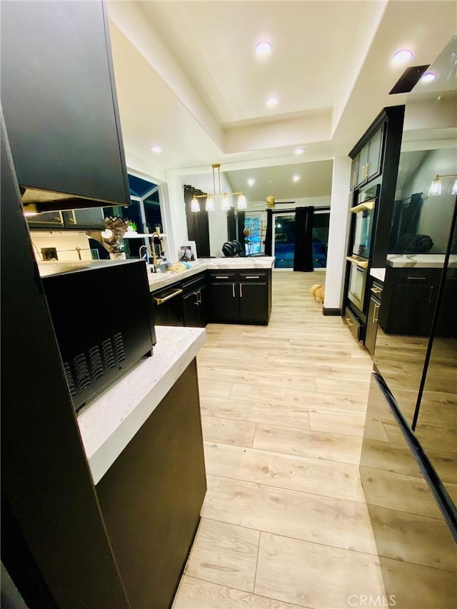 kitchen with a tray ceiling, kitchen peninsula, hanging light fixtures, and light hardwood / wood-style floors