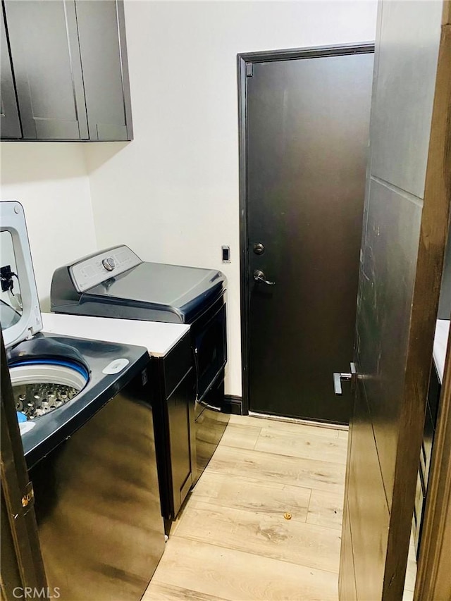 clothes washing area with light hardwood / wood-style floors, cabinets, and washing machine and clothes dryer