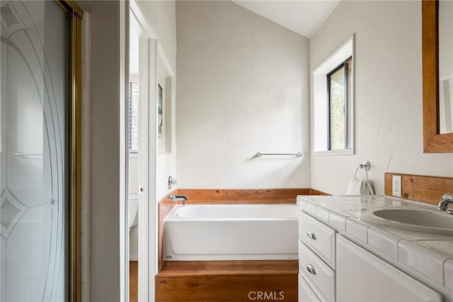 bathroom featuring vanity, toilet, a bath, and vaulted ceiling