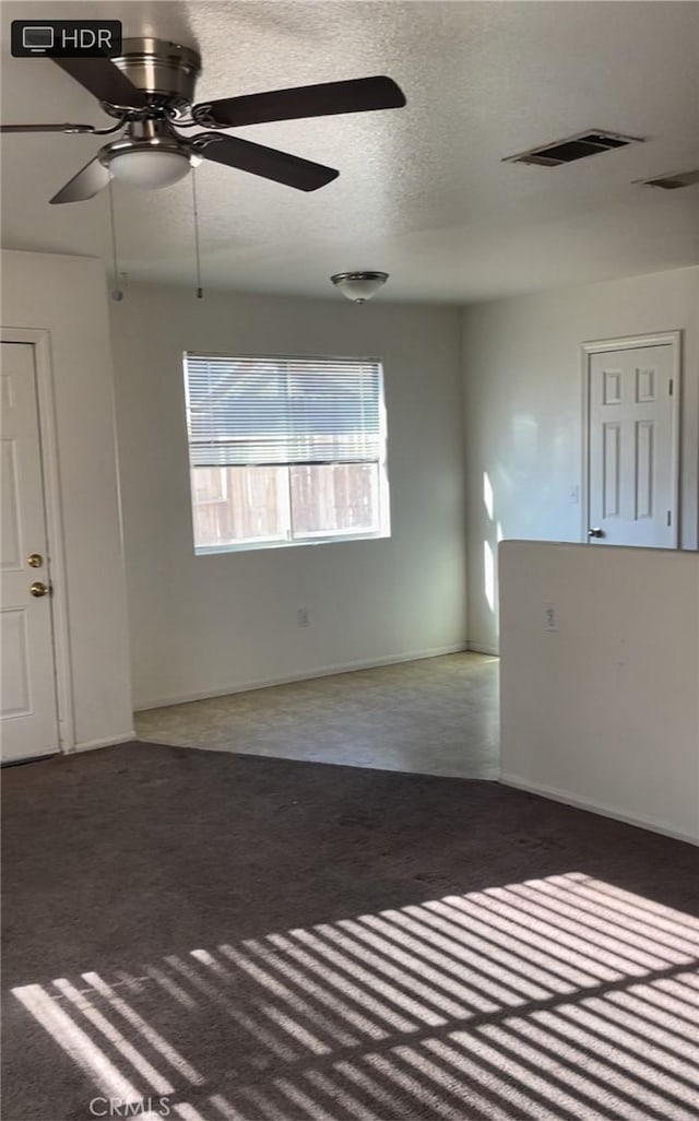 empty room with a textured ceiling, dark colored carpet, and ceiling fan