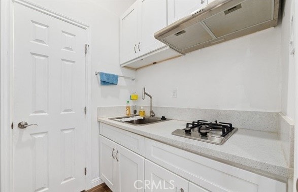 kitchen featuring stainless steel gas stovetop, exhaust hood, sink, and white cabinetry