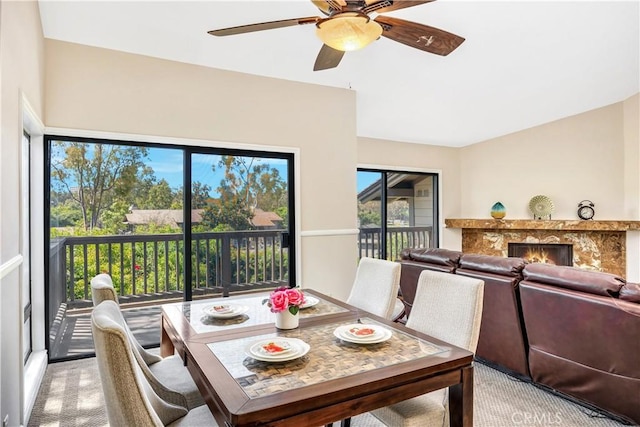 dining room featuring ceiling fan, a healthy amount of sunlight, light carpet, and a high end fireplace