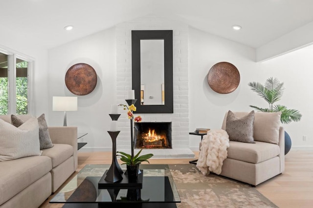 living room with lofted ceiling, a brick fireplace, and light hardwood / wood-style floors