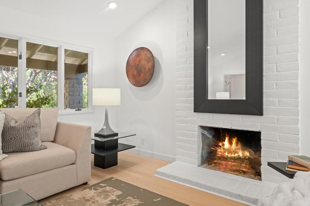 living room with a brick fireplace, lofted ceiling, and light wood-type flooring