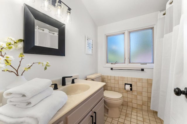 bathroom featuring lofted ceiling, tile walls, vanity, toilet, and tile patterned floors