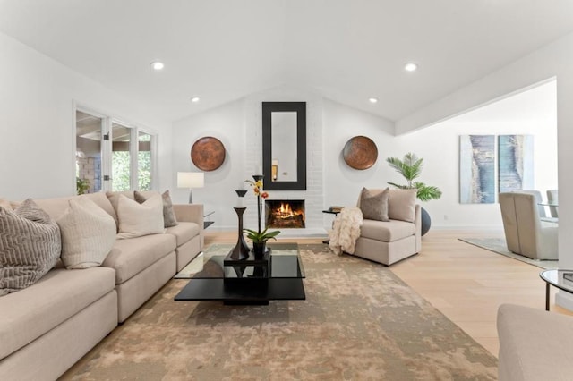 living room with lofted ceiling, a large fireplace, and light hardwood / wood-style floors