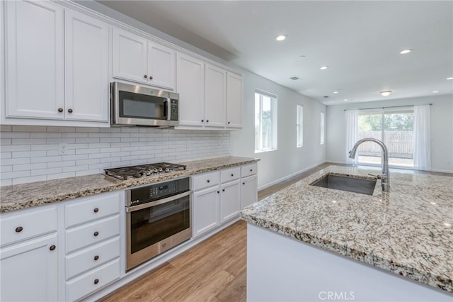 kitchen with light wood-type flooring, tasteful backsplash, sink, white cabinets, and appliances with stainless steel finishes